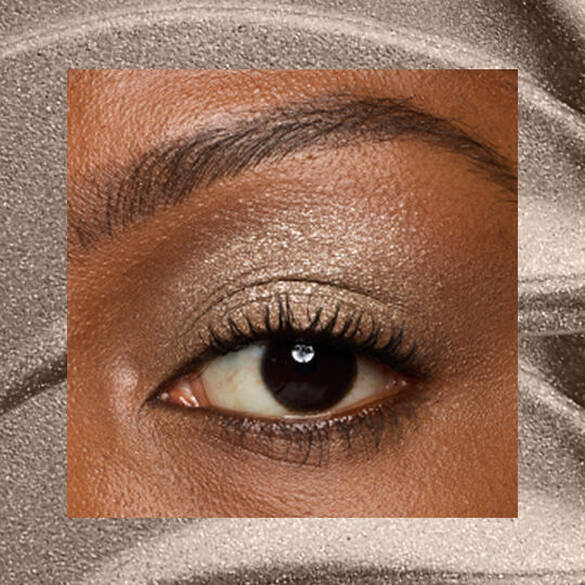 Close-up of an eye area with NYX Professional Makeup Lid Lingerie Cream Eye Pigment in 07 Granite Grind, shown on a brown shimmer textured background.