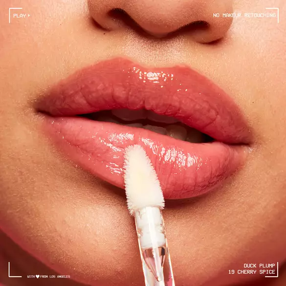 Close-up of lips being applied with a clear lip gloss called \'Duck Plump 19 Cherry Spice,\' showcasing a glossy finish.