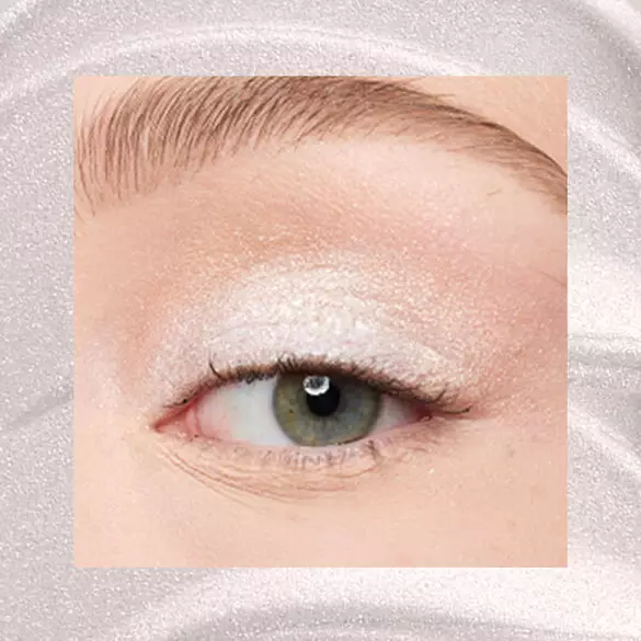 Close-up of an eye area with NYX Professional Makeup Lid Lingerie Cream Eye Pigment in 01 Satin Silver, shown on a shimmering silver textured background.