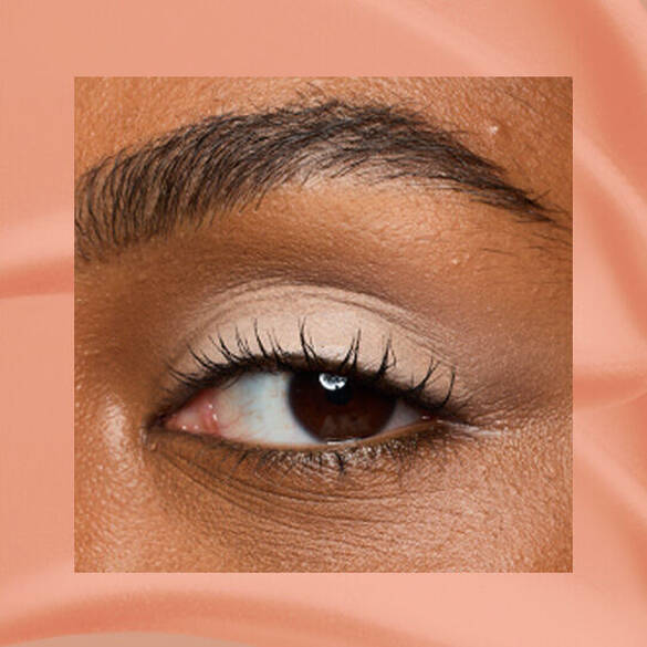Close-up of an eye area with NYX Professional Makeup Lid Lingerie Cream Eye Pigment in 02 In-Nude-Endo, shown on a nude matte textured background.