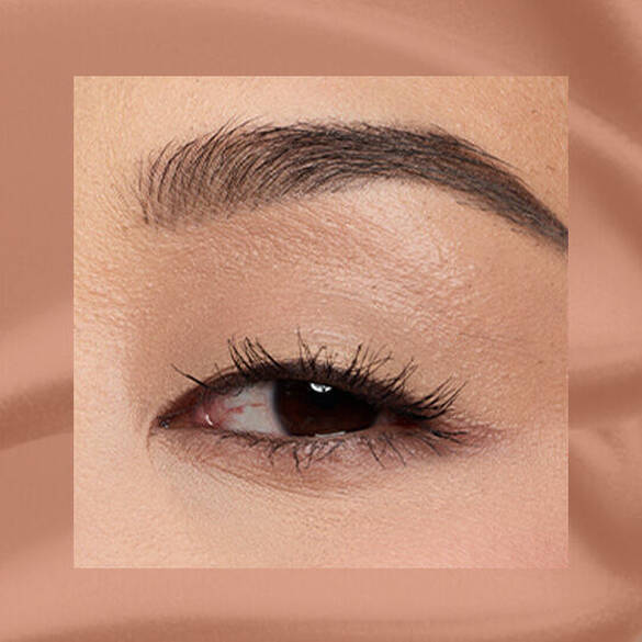 Close-up of an eye area with NYX Professional Makeup Lid Lingerie Cream Eye Pigment in 03 Beige Appeal, shown on a tan matte textured background.