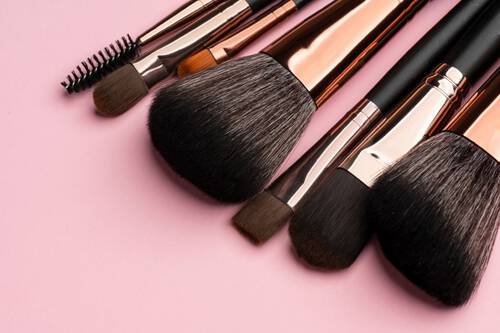 Pędzle do makijażu z czarnymi trzonkami i złotymi skuwkami ułożone na rożowym tle