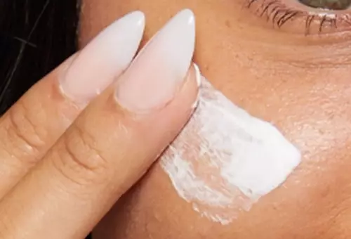 Zbliżenie na kobiecą twarz i dłonie, ktore aplikują The Marshmellow Smoothing Primer NYX Professional Makeup