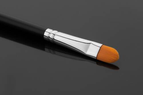 Płaski pędzelek do makijażu ze srebrną skuwką i płaską końcowką na czarnym tle