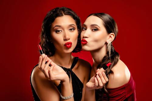 Zbliżenie na twarze dwoch przyjaciołek, ktorych usta pomalowane są w odcieniu intensywnej chłodnej czerwieni