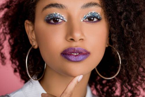 Kobieta w makijażu na imprezę z brokatem na powiekach i fioletowymi ustami