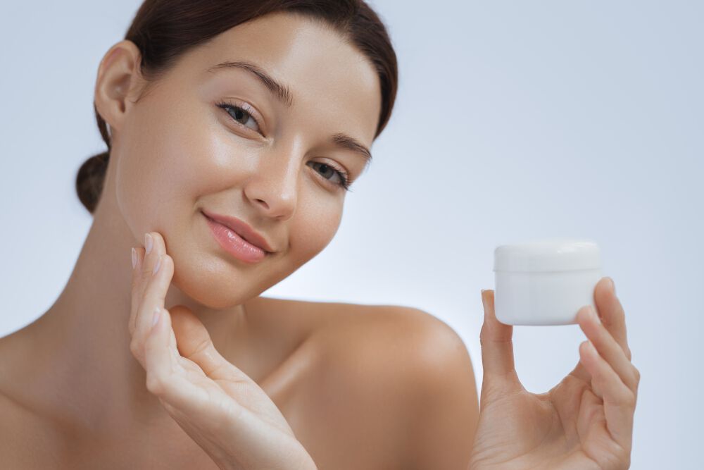 Zbliżenie na twarz kobiety, ktora nakłada krem na policzki