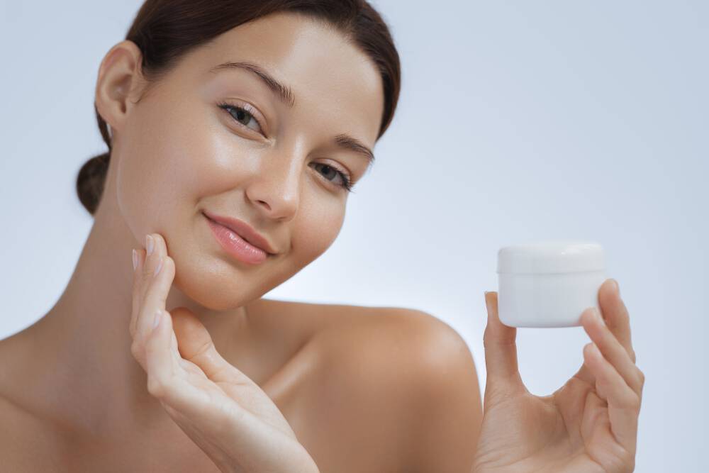 Zbliżenie na twarz kobiety, ktora nakłada krem na policzki