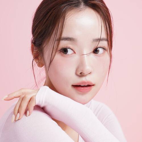 Młoda kobieta w białej bluzce i z upiętymi włosami na rożowym tle, oglądająca się przez ramię