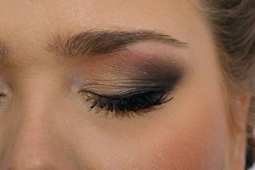 Fragment kobiecej twarzy z zamkniętym okiem, wyregulowaną brwią i makijażem w stylu smoky eyes.