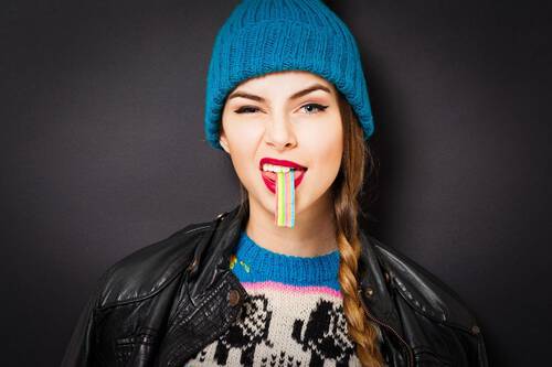 Młoda kobieta je tęczowego żelka, na oczach ma mocne, graficzne kreski