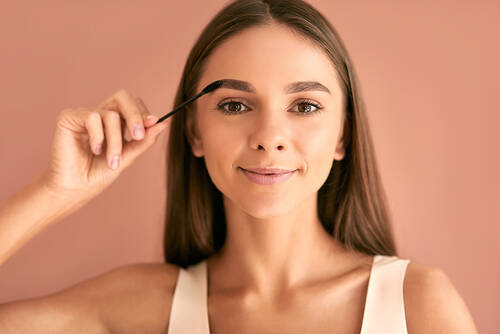 Młoda kobieta trzyma szczoteczkę do stylizacji i malowania brwi i uśmiecha się