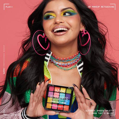 Uśmiechnięta młoda kobieta w kolorowym makijażu trzyma w dłoniach paletę Ultimate Shadow Palette