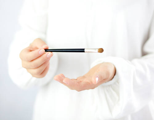 Osoba w białym stroju na białym tle trzyma w dłoniach profesjonalny pędzel do makijażu oczu.