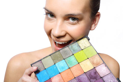 Uśmiechnięta kobieta na białym tle z kolorową paletą cieni.