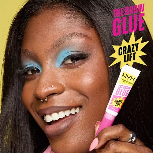 Ciemnoskora kobieta w niebieskim makijażu oczu prezentuje tubkę The Brow Glue od NYX PM