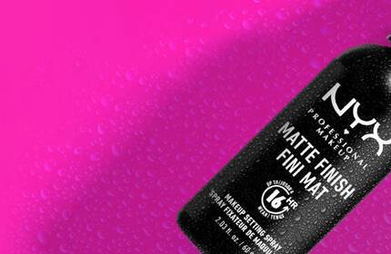 Czarny spray do makijażu NYX na rożowym tle z kroplami wody.