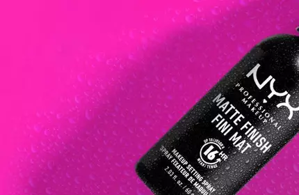 Czarny spray do makijażu NYX na rożowym tle z kroplami wody.