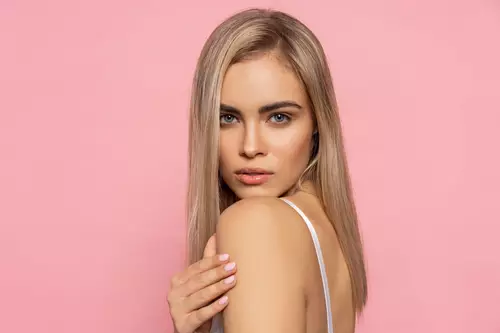 Portret kobiety z prostymi długimi włosami w kolorze blond na jasnym pastelowym tle.